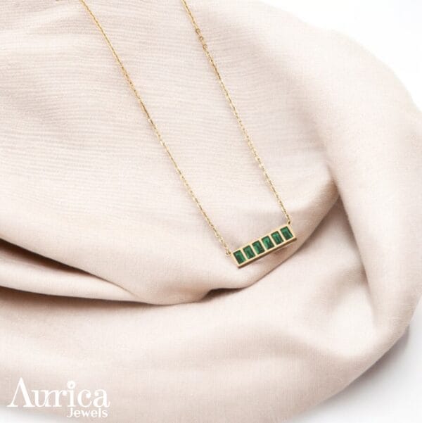The Emerald Horizon Metallic Pendant is a perfect blend of contemporary design and timeless sophistication. Its linear arrangement of emerald-green stones exudes balance and refinement.